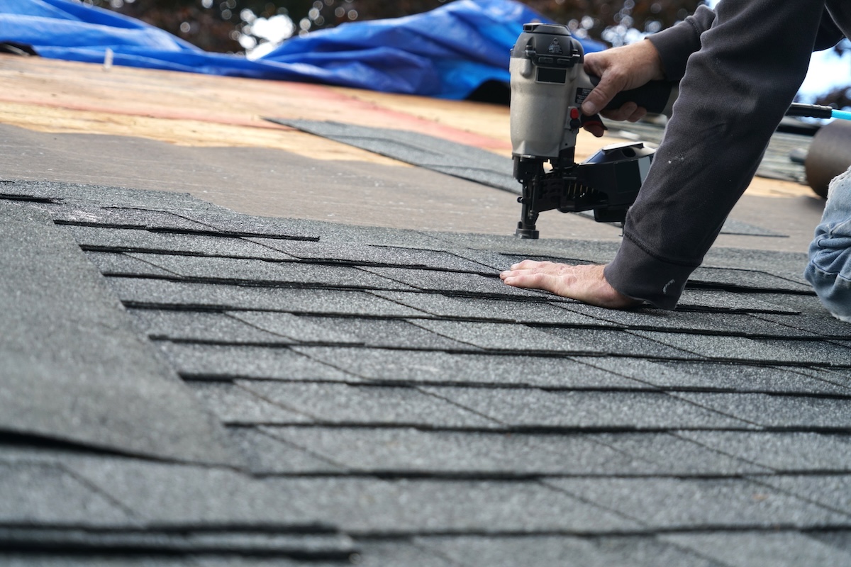 Close-up of a roofer nailing down architectural asphalt shingles during a repair
