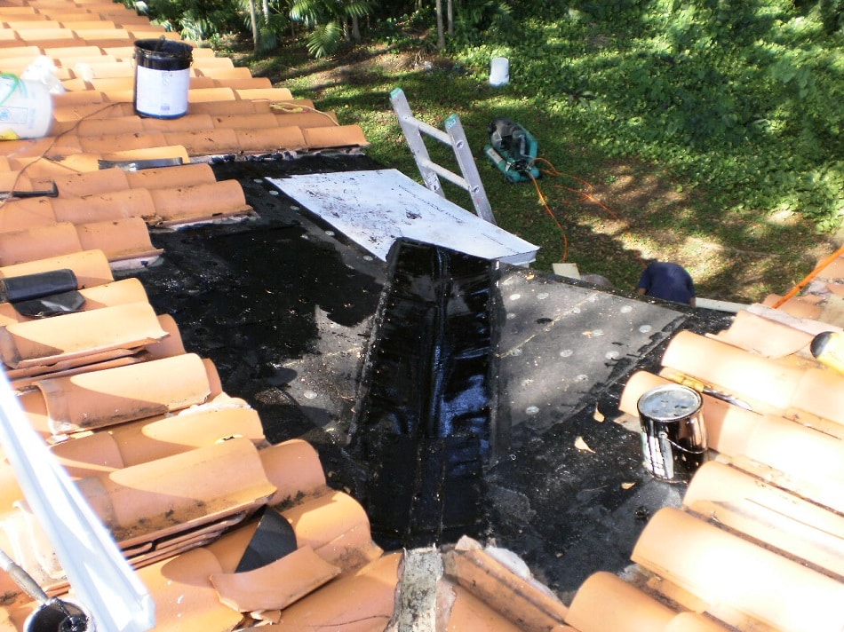 Low-slope hot-mopped roof section with new metal flashing being installed between tile fields