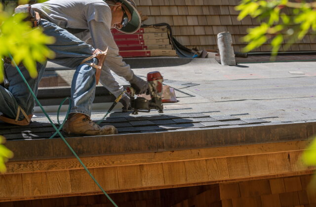 Roofer nailing new asphalt shingles into a repaired section of roof deck